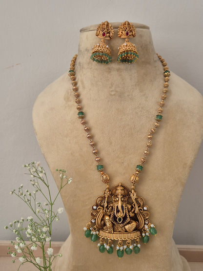 A gold-plated long necklace featuring an intricate Lord Ganesha temple pendant with dangling green beads with matching jhumka earrings by naitri.in