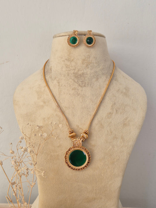 Bhavana Necklace Set in antique gold finish featuring a green stone pendant and matching stud earrings by Naitri.in