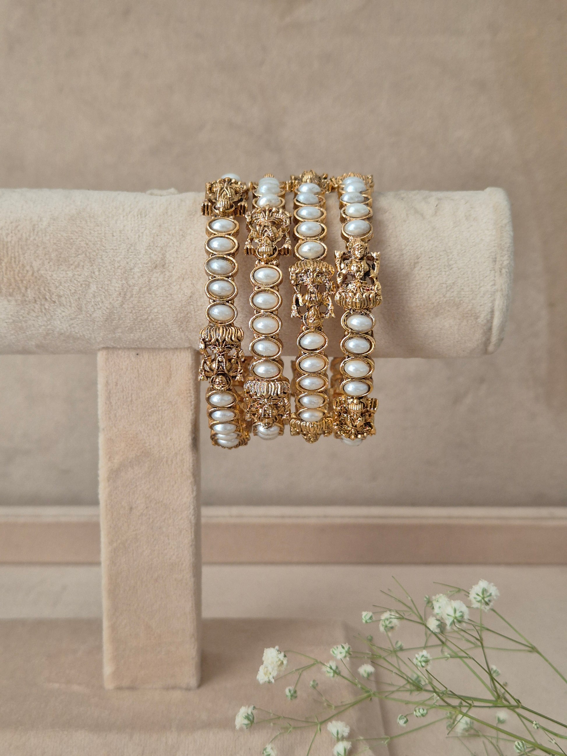 A stack of gold-toned bangles adorned with white faux pearls and intricate gold filigree, by naitir.in