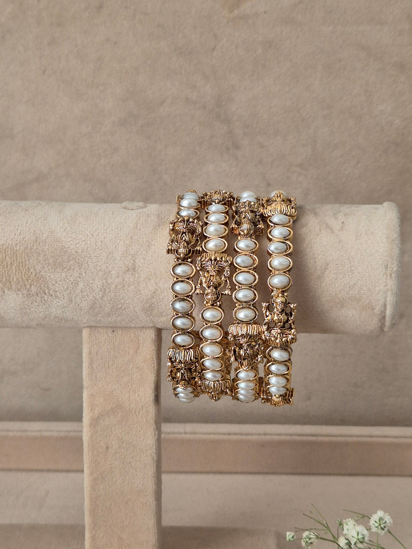 A stack of three wide gold bangles decorated with white faux pearls and intricate gold filigree, by naitri.in