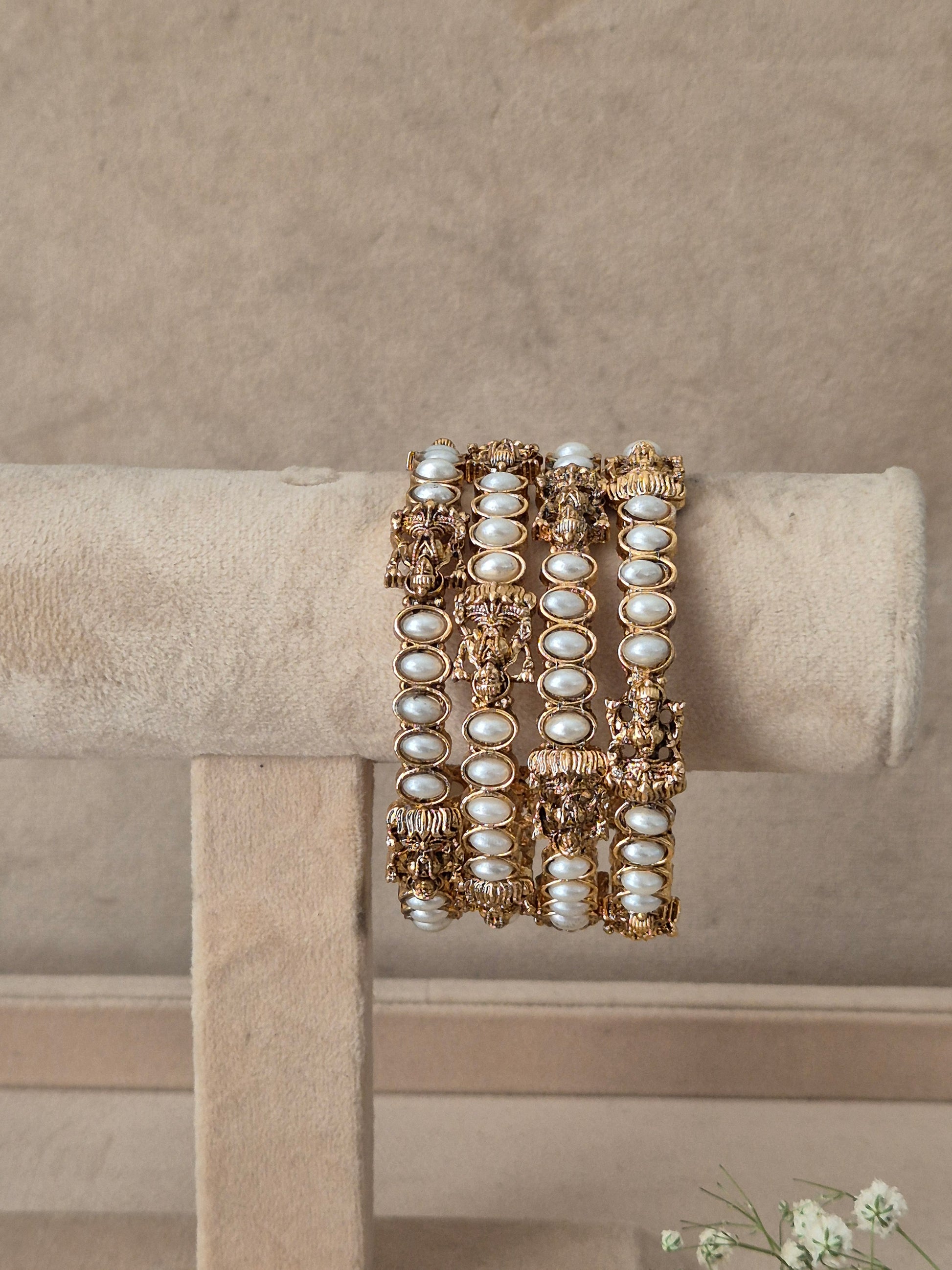 A stack of three wide gold bangles decorated with white faux pearls and intricate gold filigree, by naitri.in