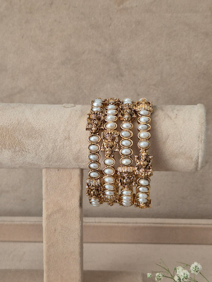 A stack of three wide gold bangles decorated with white faux pearls and intricate gold filigree, by naitri.in