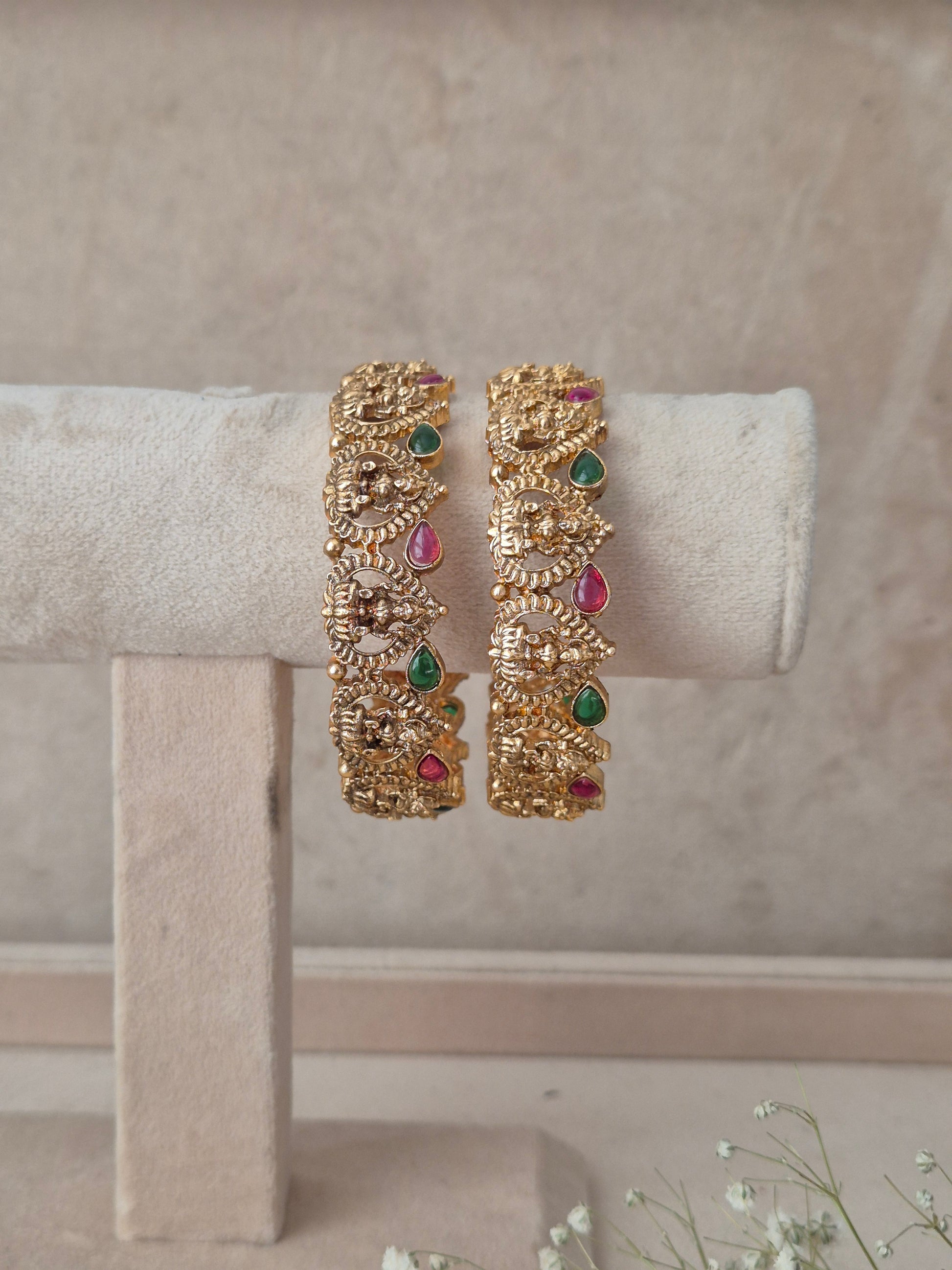 Traditional gold-finish kangan set of 2 with carved goddess motifs, teardrop ruby red and emerald green stones by naitri.in