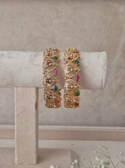 Traditional gold-finish kangan set of 2 with carved goddess motifs, teardrop ruby red and emerald green stones by naitri.in