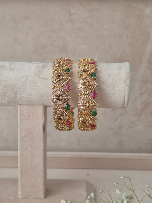 Traditional gold-finish kangan set of 2 with carved goddess motifs, teardrop ruby red and emerald green stones by naitri.in