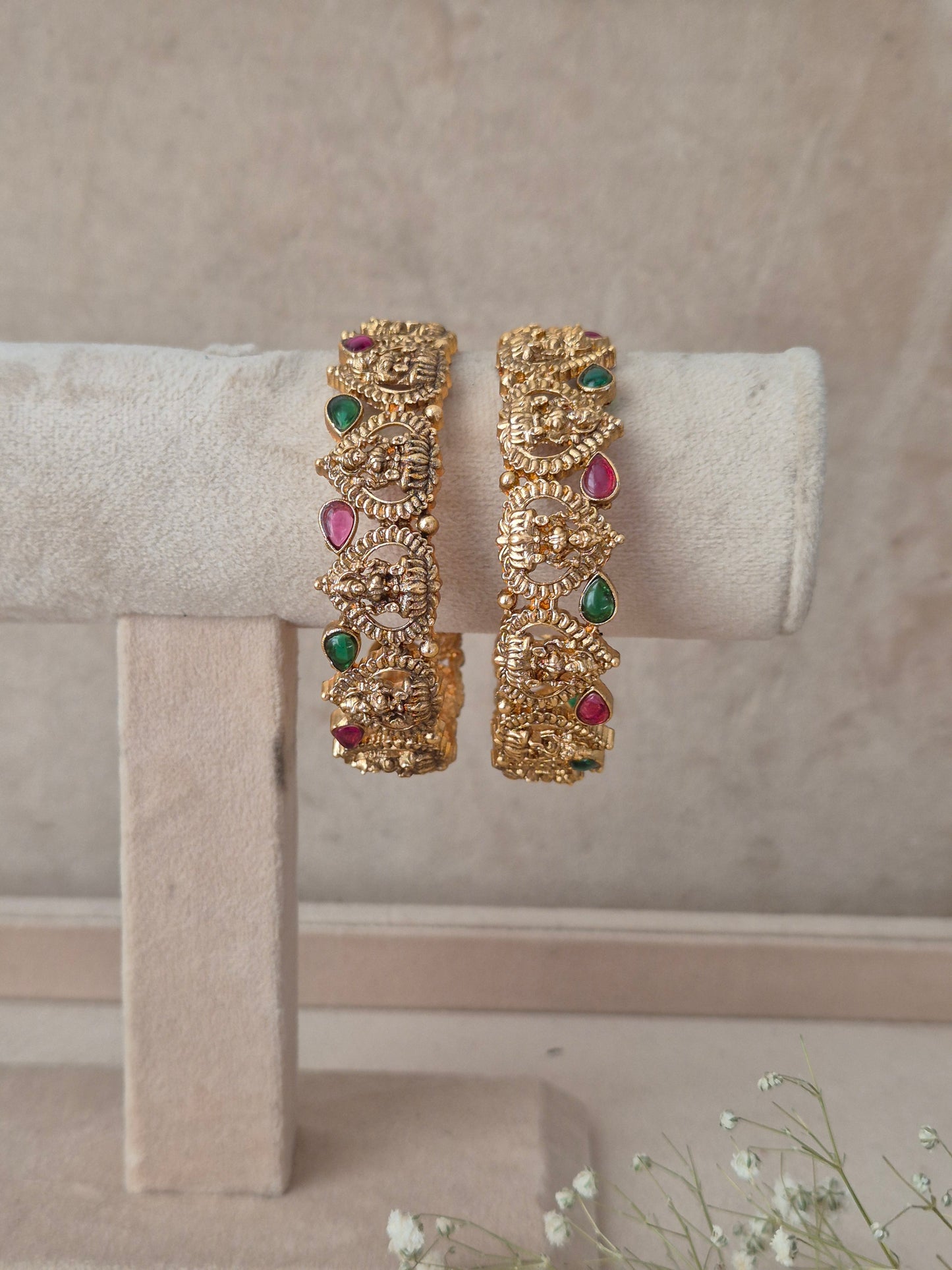 Festive antique gold bangle pair featuring carved temple motifs and colorful stone accents for wedding and traditional wear Antique gold-plated ethnic temple jewelry bangles with red and green stone detailing by naitri.in