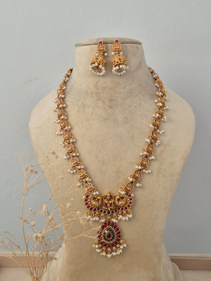 Bhuvneshwari Antique Gold Long Necklace Set displayed on a beige mannequin bust, showcasing intricate traditional temple craftsmanship with rich ruby stone accents and matching jhumka earrings by Naitri.in