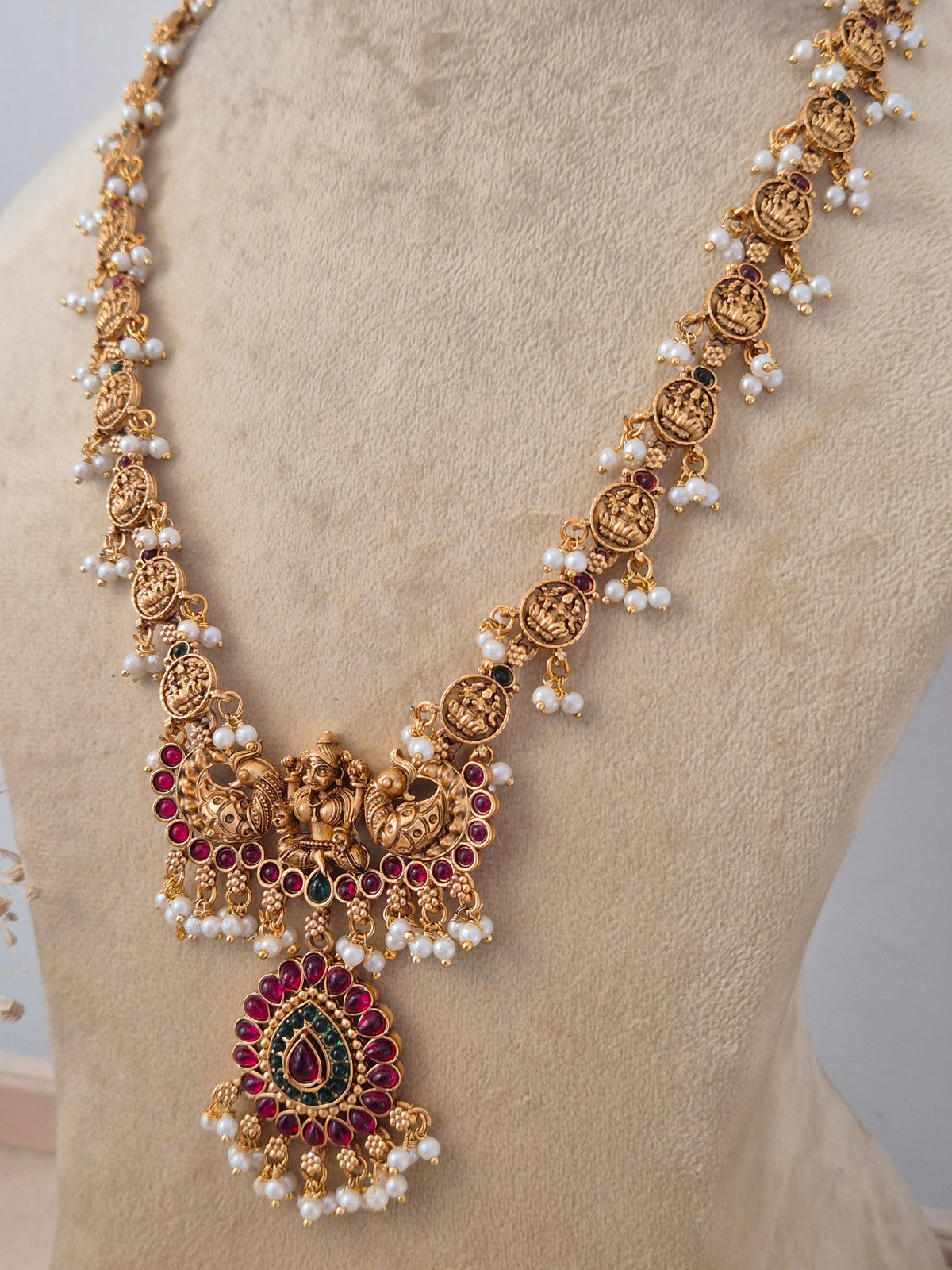 Ornate Cultural Long Necklace and Jhumkas presented on a display bust, emphasizing the classic royal motifs, polished antique gold finish, and traditional elements ideal for festive styling by naitri.in