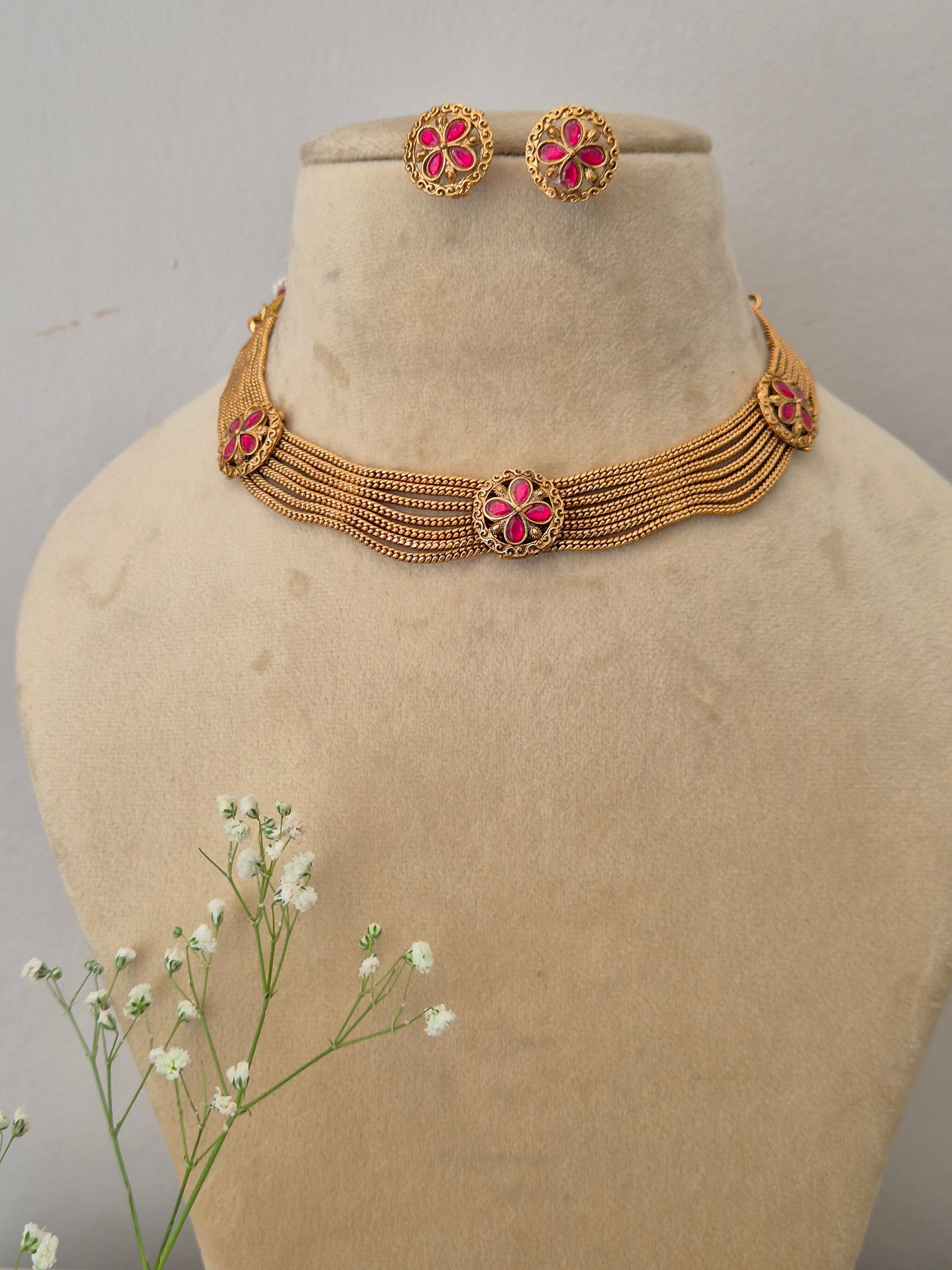 Elegant gold-toned Indian choker necklace set with pink floral details, styled with delicate white flowers by naitri.in