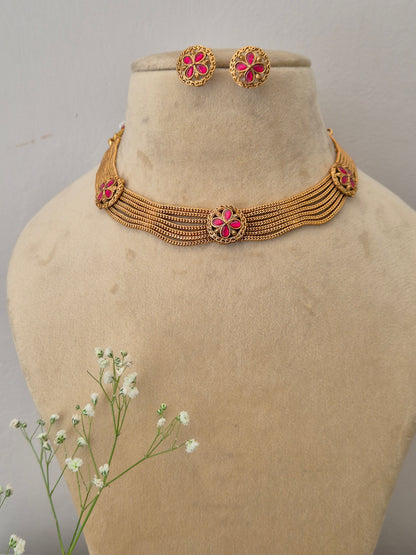 Elegant gold-toned Indian choker necklace set with pink floral details, styled with delicate white flowers by naitri.in