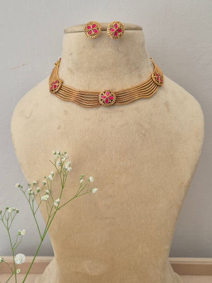 Bina Necklace Set A gold-plated multi-strand choker necklace featuring pink floral gemstone embellishments and matching stud earrings by naitri.in