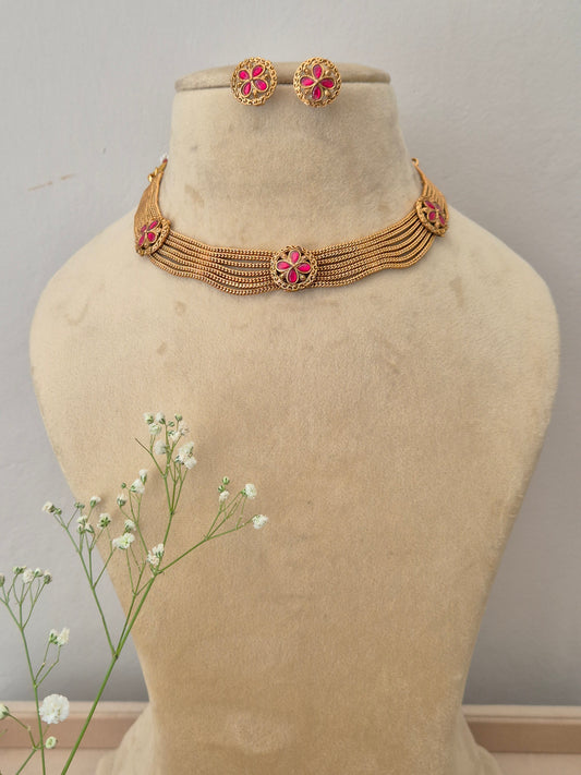 Bina Necklace Set A gold-plated multi-strand choker necklace featuring pink floral gemstone embellishments and matching stud earrings by naitri.in