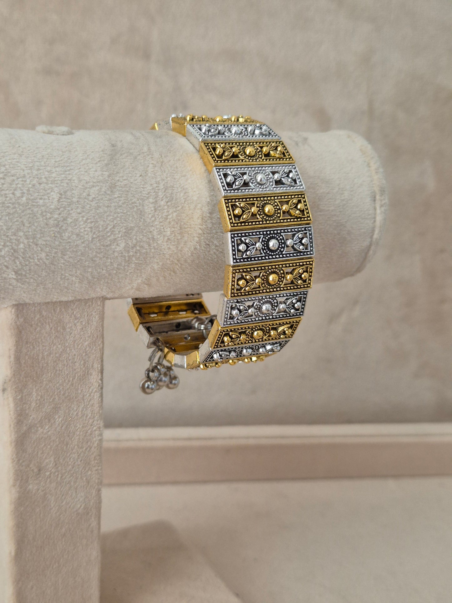 Wide statement Kada bangle featuring intricate horizontal bands of gold-toned patterns and silver-plated filigree panels by naitri.in