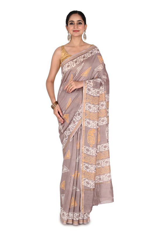 A model wearing the greyish-mauve cotton-silk saree featuring traditional white and gold hand-block printed floral patterns, styled with a sleeveless gold blouse by naitri.in