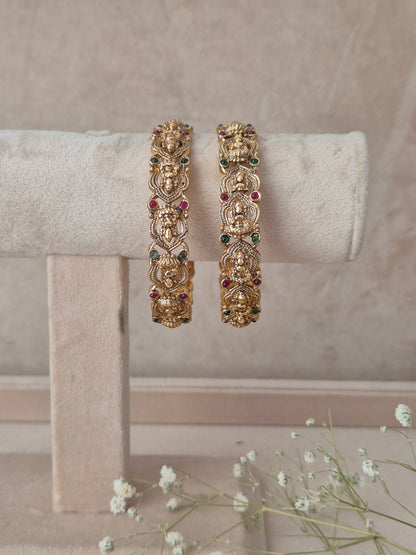 Two gold-toned traditional Indian bangles with detailed filigree work and small multicolored stone accents, by naitri.in