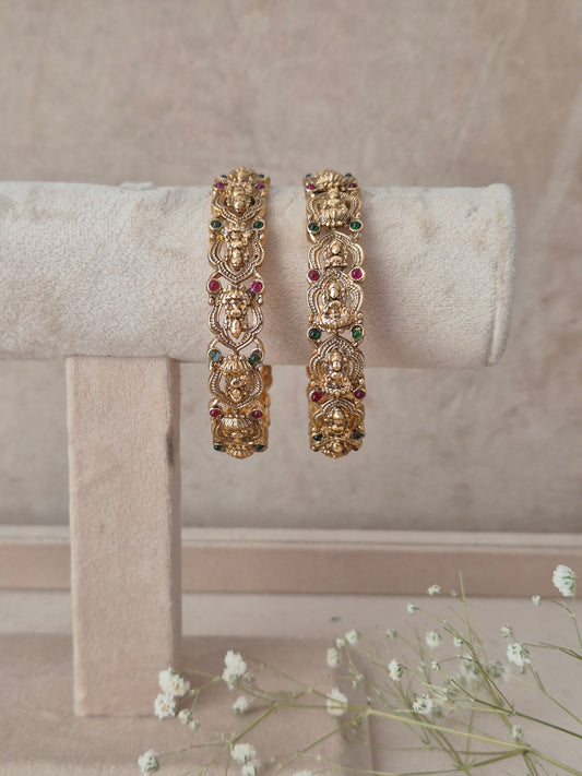 Two gold-toned traditional Indian bangles with detailed filigree work and small multicolored stone accents, by naitri.in