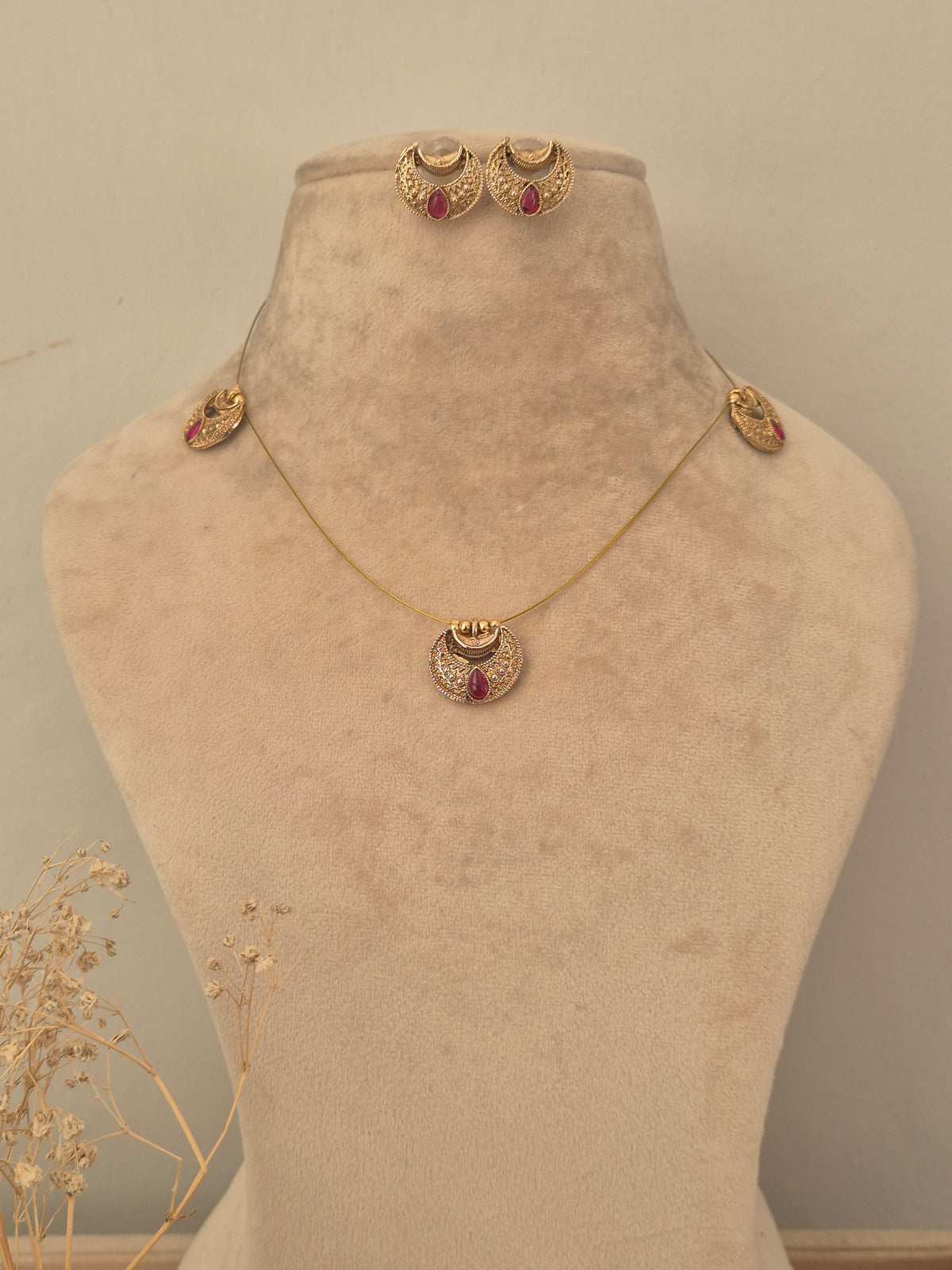 Gold invisible chain necklace featuring crescent-shaped stations, a central circular pendant with a red stone accent,  with matching crescent stud earrings by naitri.in
