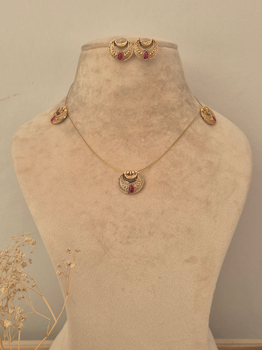 Gold invisible chain necklace featuring crescent-shaped stations, a central circular pendant with a red stone accent,  with matching crescent stud earrings by naitri.in
