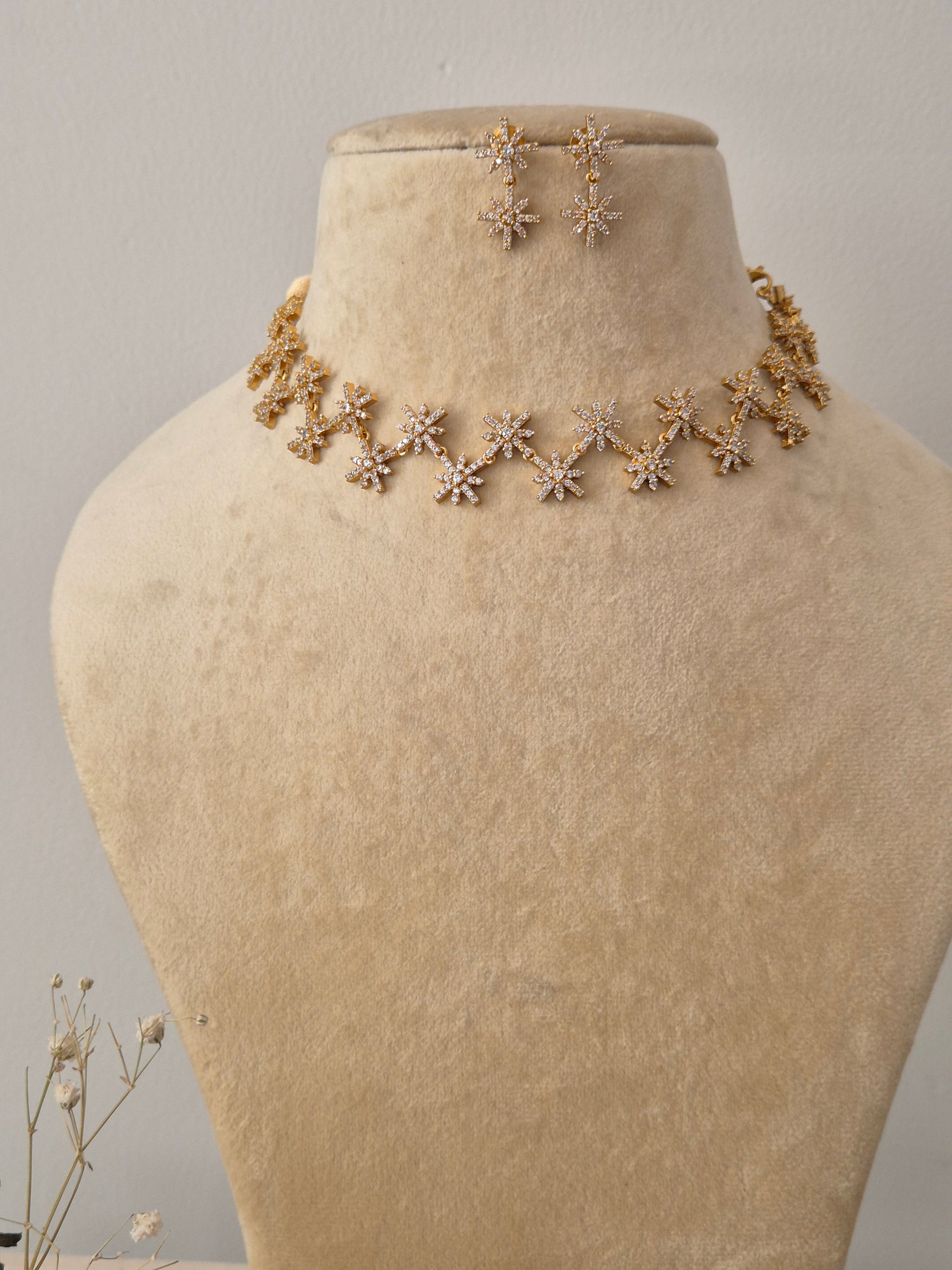 Necklace Set featuring a gold-toned choker with interlocking star-shaped motifs, American diamond accents, and matching starburst stud-drop earrings by naitri.in