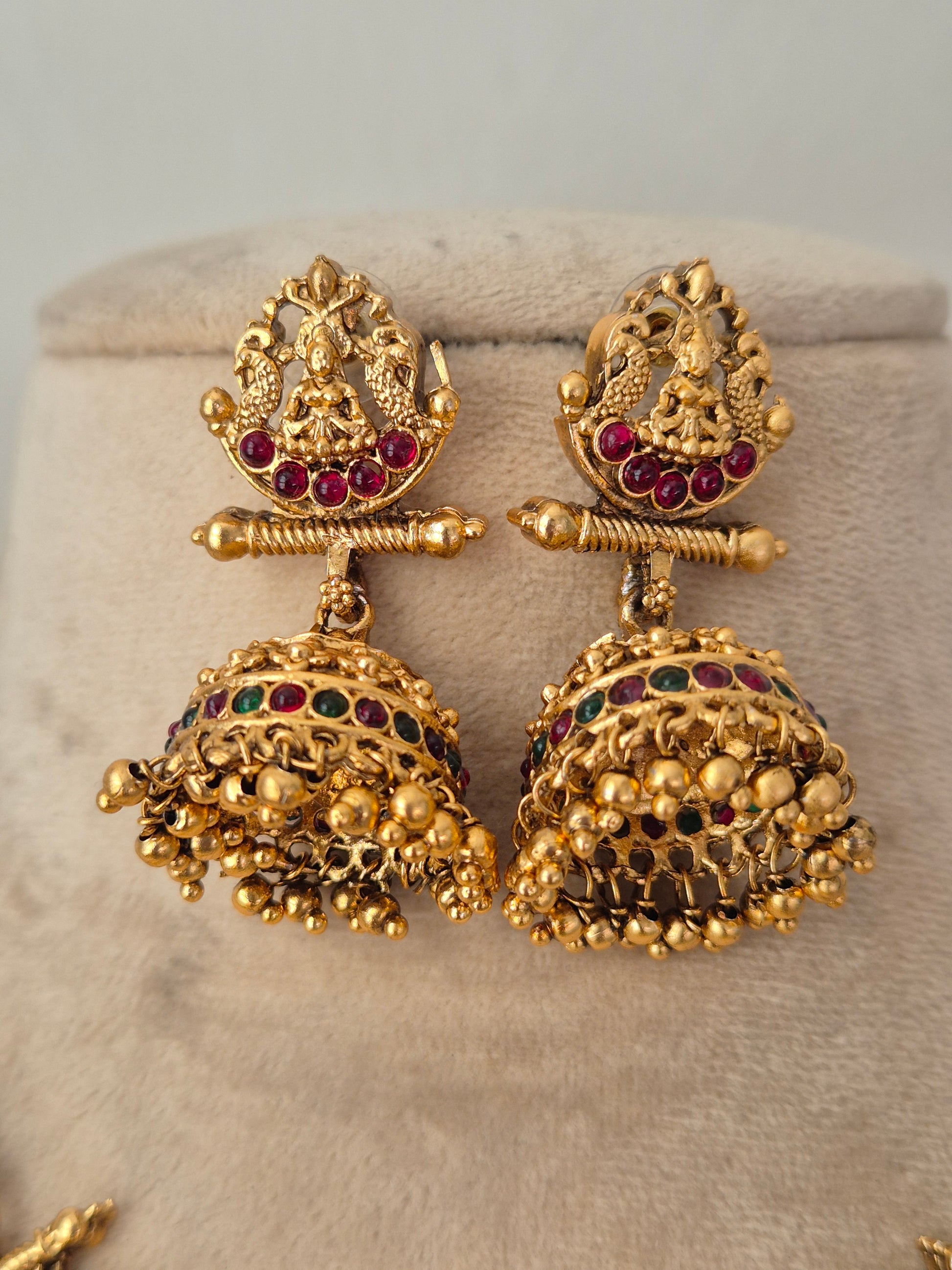 A pair of ornate gold-toned traditional Indian jhumka earrings with red and green stone accents,  by naitri.in
