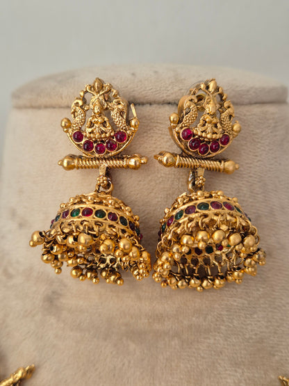 A pair of ornate gold-toned traditional Indian jhumka earrings with red and green stone accents,  by naitri.in