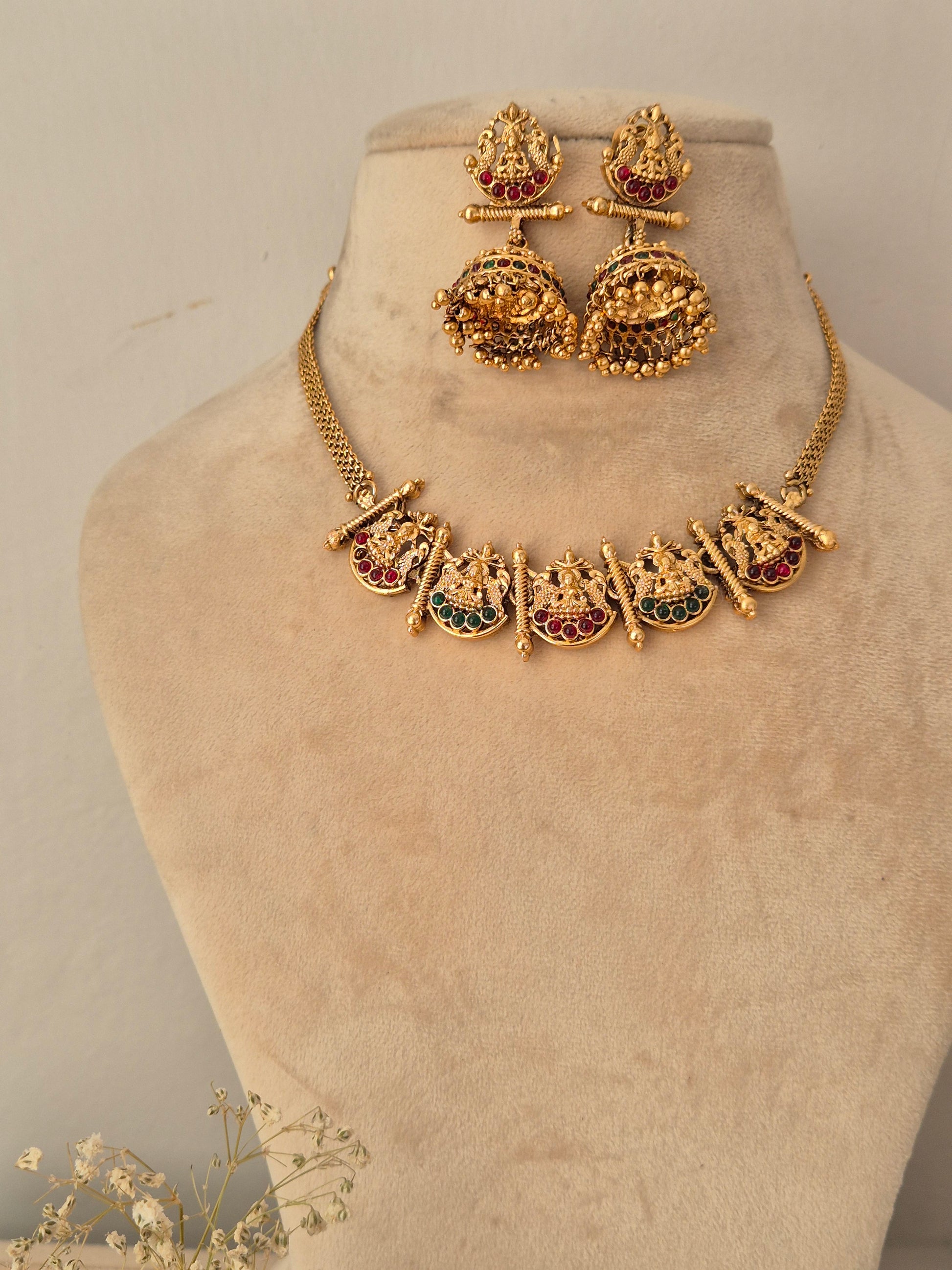 Gold-toned traditional jewelry set, including a necklace with decorative pendant and matching earrings with red and green stone accents by naitri.in
