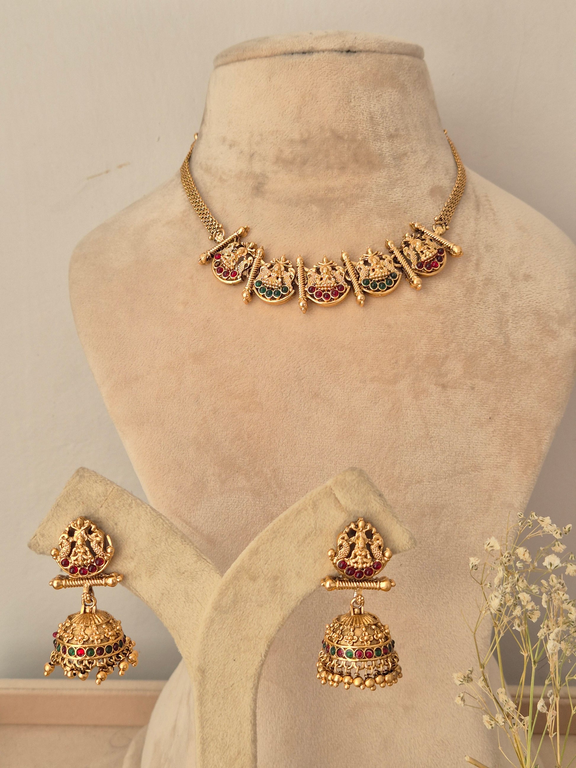 Gold-toned traditional jewelry set, including a necklace with five ornate pendant motifs and matching drop earrings, accented with red and green stones by naitri.in