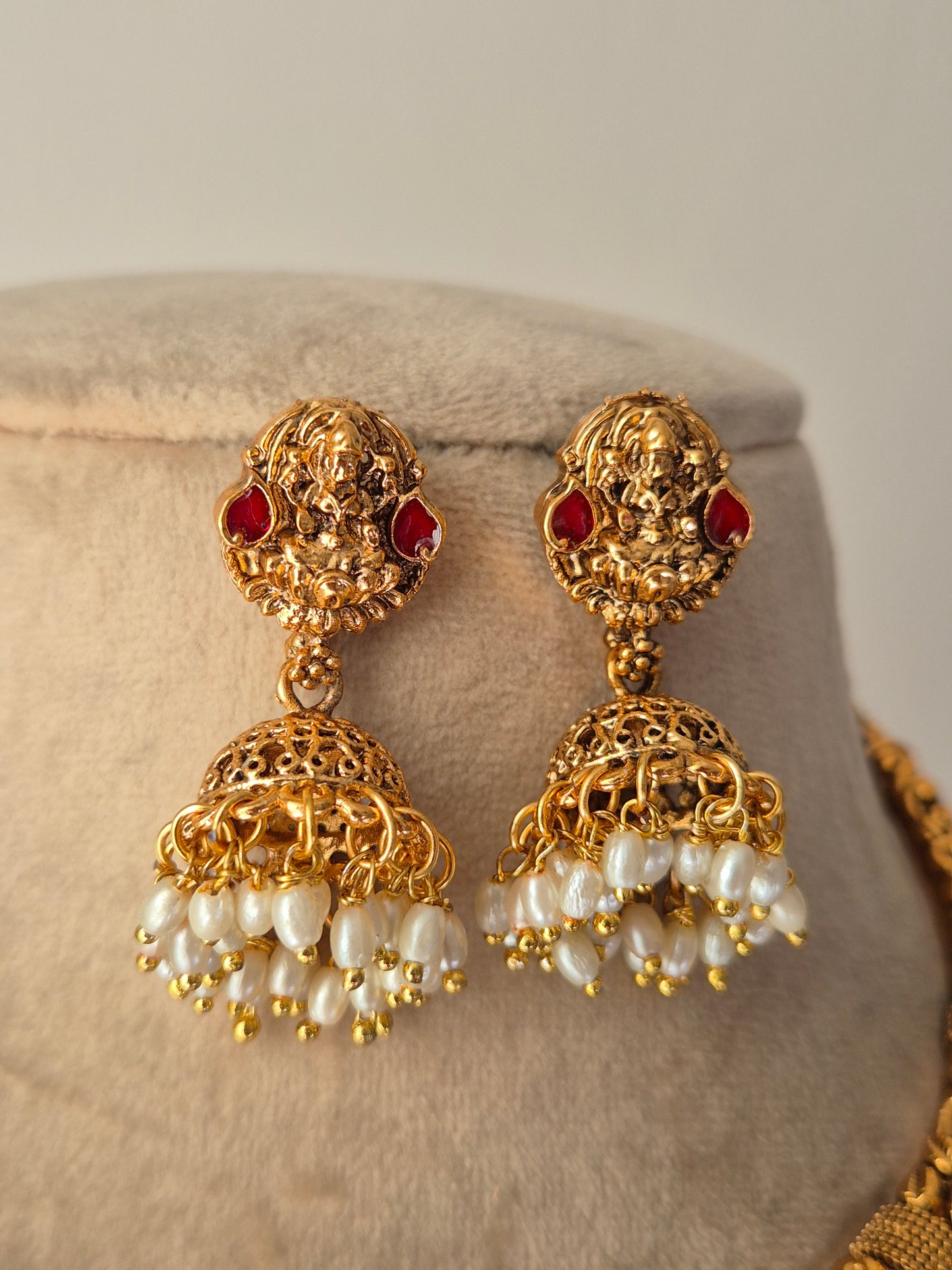 Gold earrings  with goddess motif design and red stones and pearl-like beads hanging from jhumkas  by naitri.in