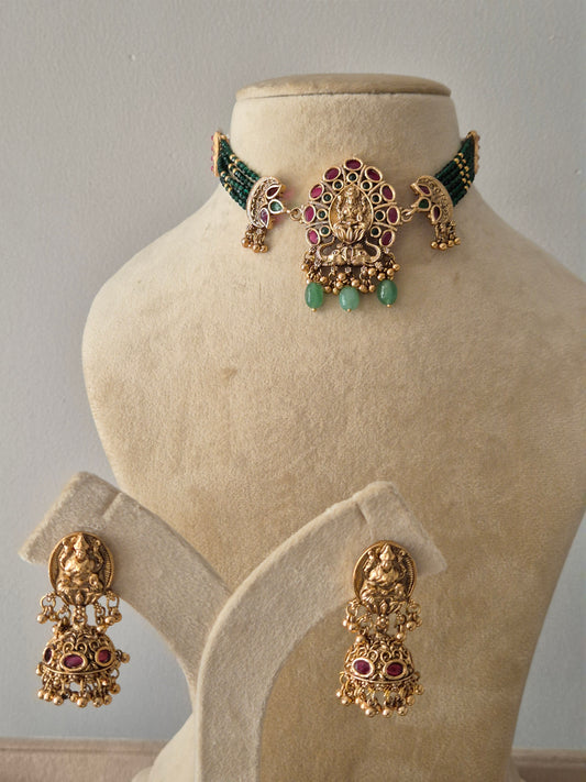 Handcrafted temple jewellery choker set featuring a gold-toned Lakshmi pendant with pink stones and green bead droplets, paired with matching jhumka earrings by naitri.in