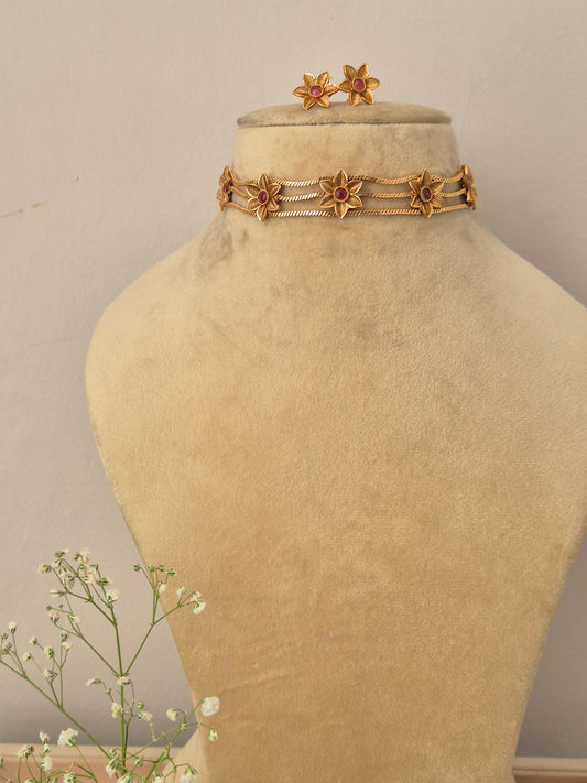 A gold-plated ethnic choker necklace featuring detailed floral filigree patterns with pinkish-red ruby stone centers, matching flower stud earrings by naitri.in