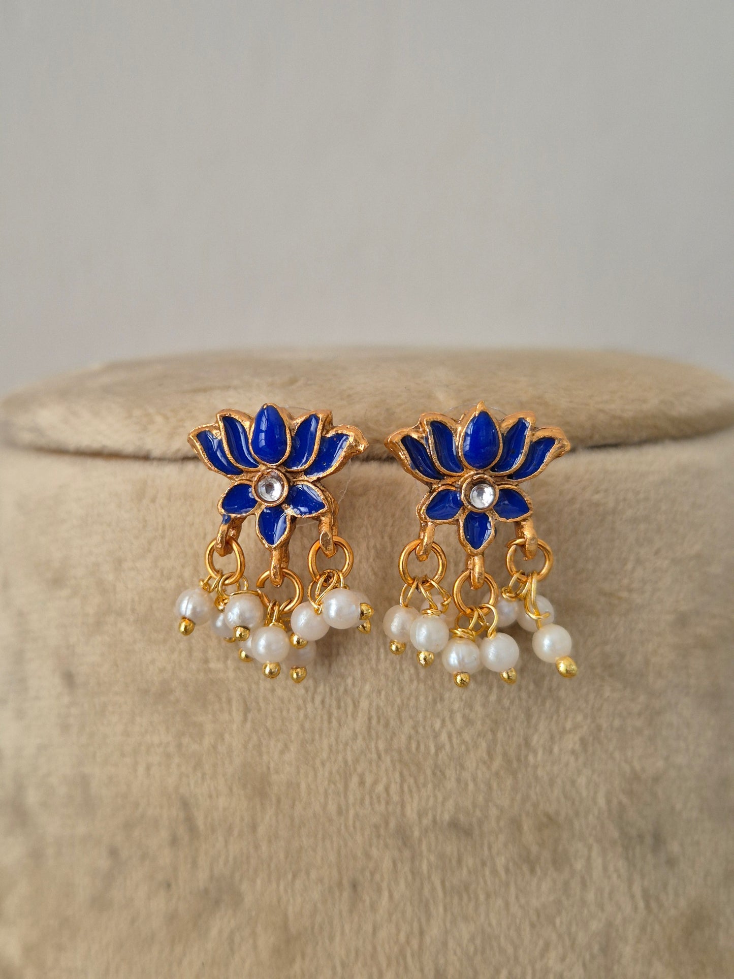 A pair of gold-plated earrings with blue enamel lotus flowers, small white pearl centers, and dangling pearl chains, by naitri.in