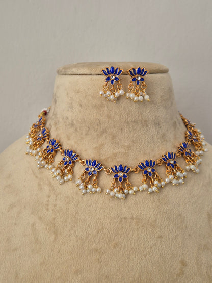Gold-toned floral jewelry set with blue enamel flowers and small white pearl accents, Handcrafted antique gold statement jewelry set showcasing blue stone embellishments and tiny hanging seed pearls, ideal for festive and bridal styling by naitri.in