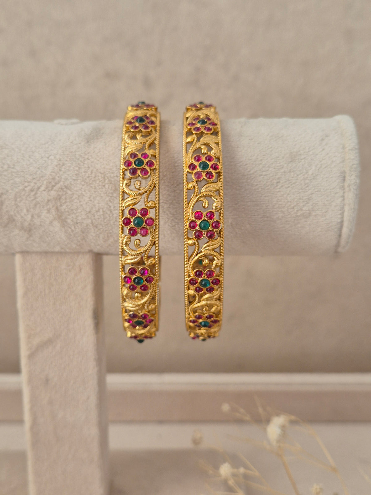 Set of 2 gold-plated bangles featuring delicate floral jaal scrollwork studded with ruby red and emerald green stones by naitri.in