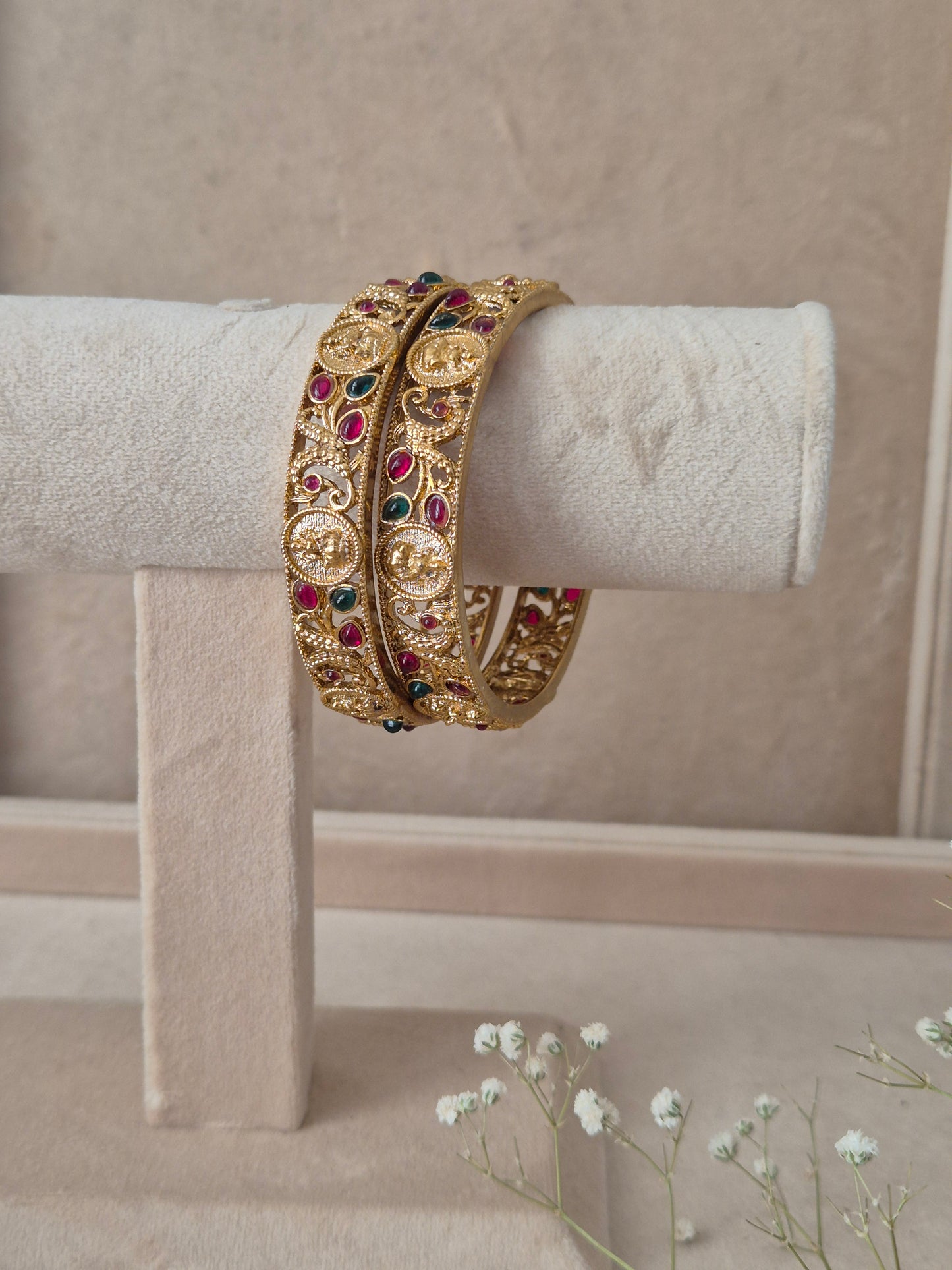 Pair of Naitri's Chirasvi gold bangles showcasing detailed ethnic craftsmanship, embedded with vibrant pinkish-red and green accent stones by naitri.in