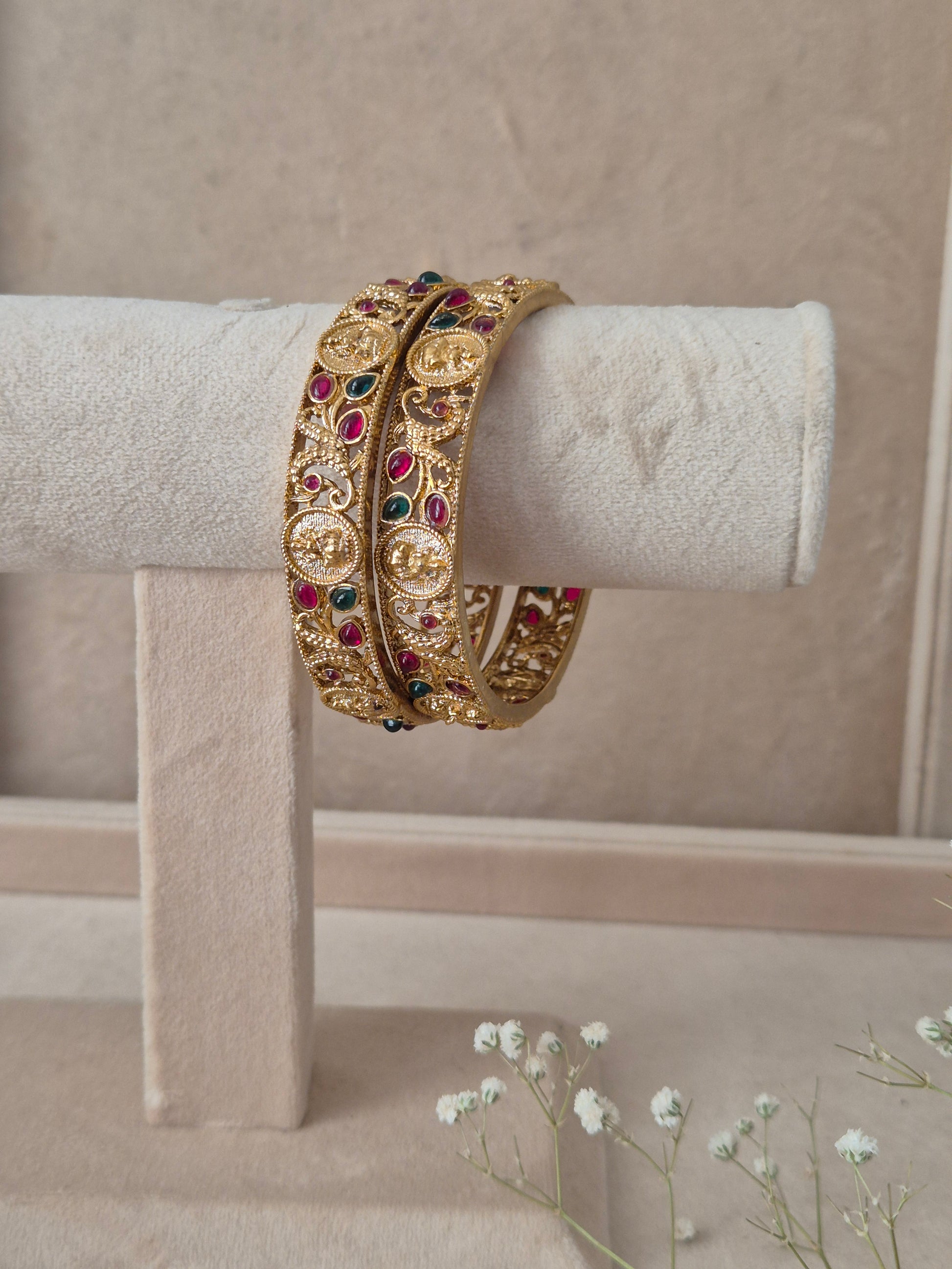 Pair of Naitri's Chirasvi gold bangles showcasing detailed ethnic craftsmanship, embedded with vibrant pinkish-red and green accent stones by naitri.in