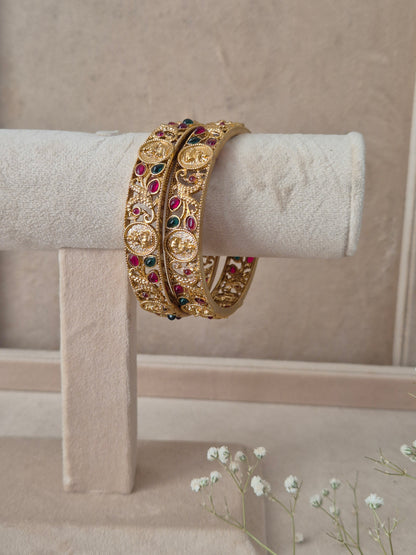 Pair of Naitri's Chirasvi gold bangles showcasing detailed ethnic craftsmanship, embedded with vibrant pinkish-red and green accent stones by naitri.in