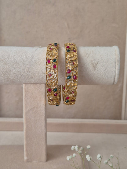 Set of 2 Chirasvi gold bangles by Naitri featuring intricate traditional engravings, accented with alternating ruby-red and emerald-green gemstones, by naitri.in