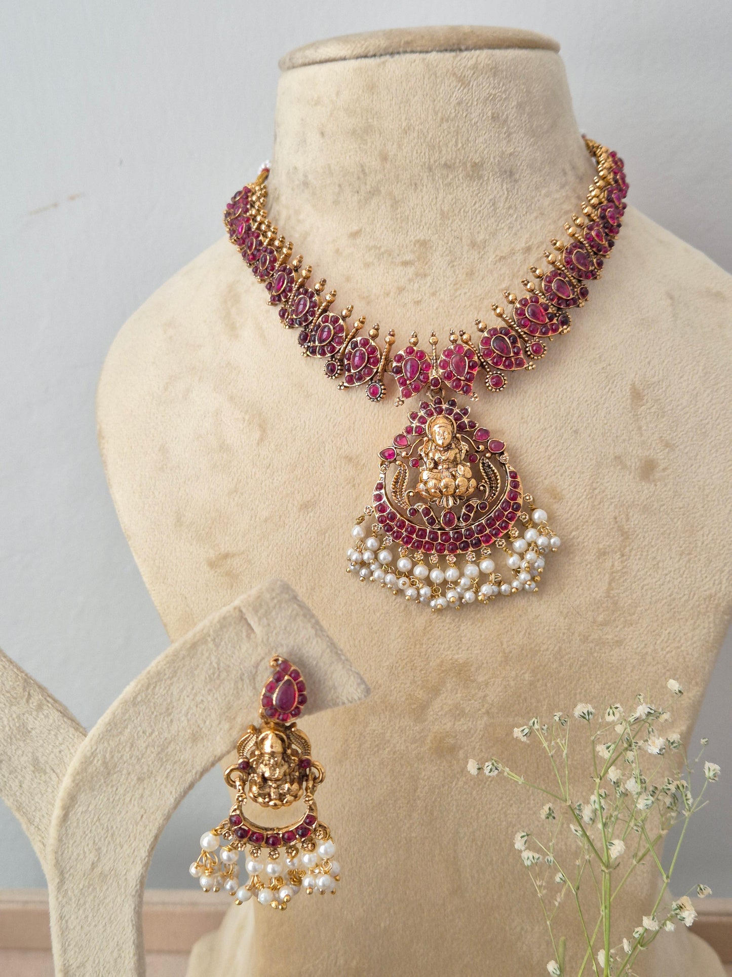 Gold-plated traditional Indian jewelry set featuring a necklace, a large pendant, and a matching earring, embellished with deep pinkish-red stones and white pearls, by naitri.in