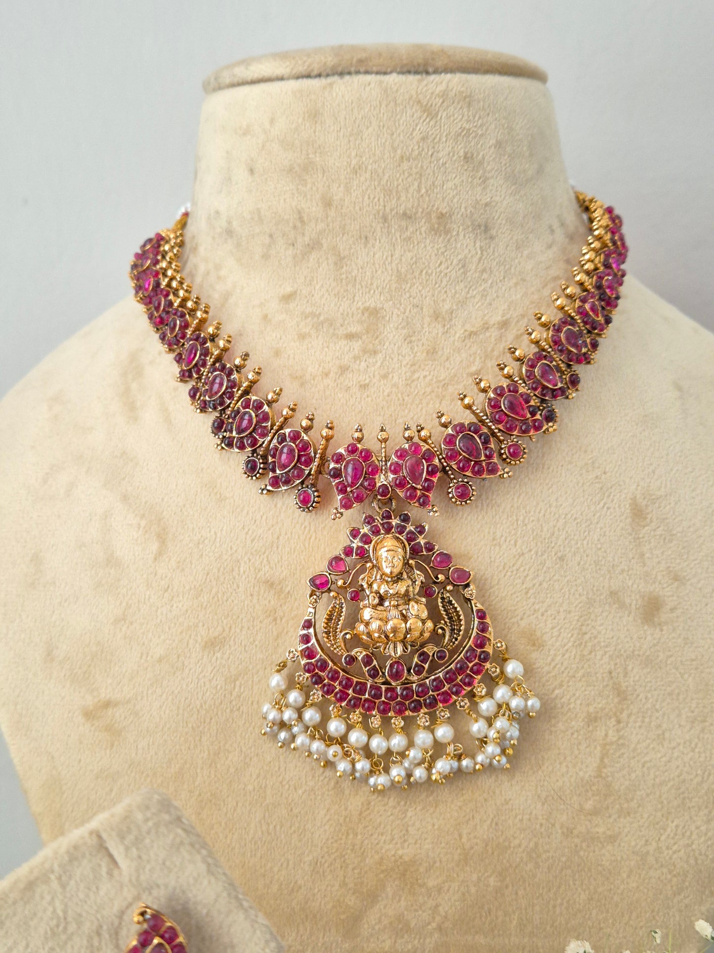An ornate Indian-style gold necklace with deep pinkish-red stones and white pearl accents, by naitri.in