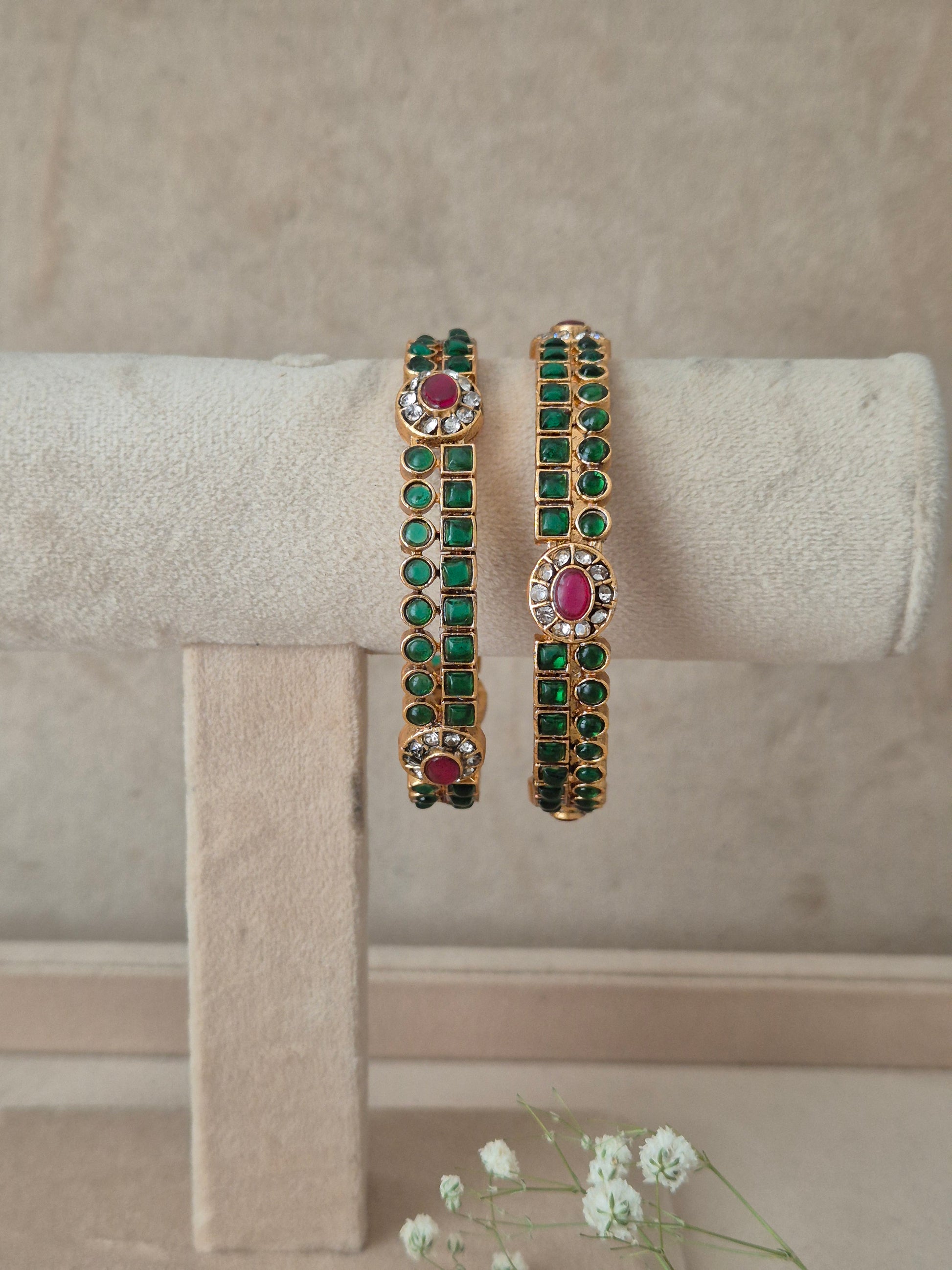 Two gold-plated bangles decorated with green stones and pink oval center stones, by naitri.in