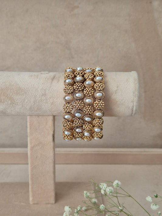 A wide gold-toned bangle bracelet with rows of white faux pearls and textured gold beadwork, by naitri.in