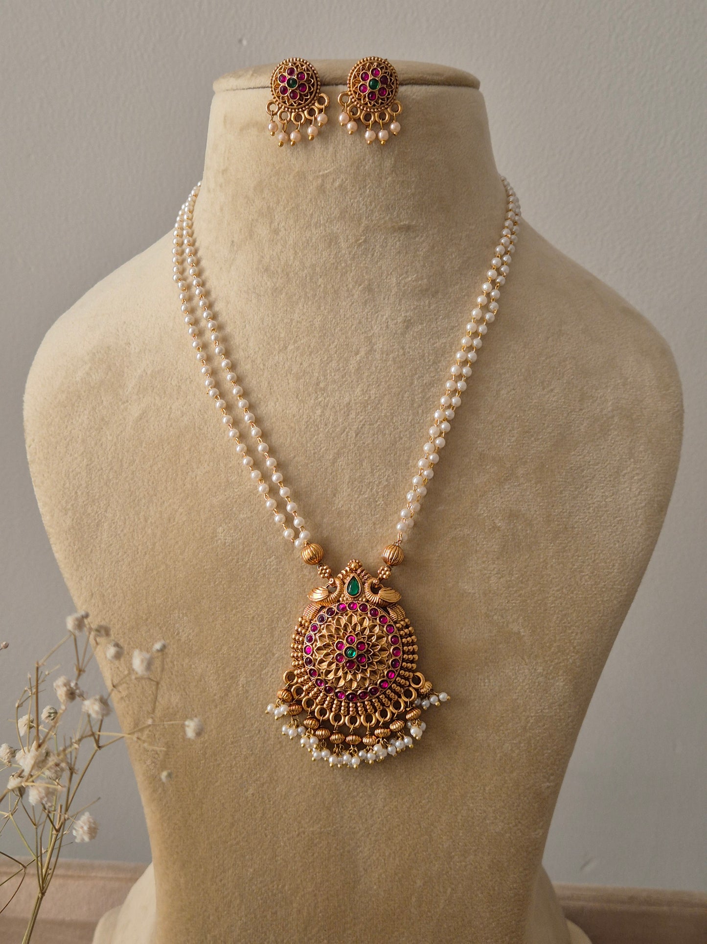 Set featuring a double-strand pearl chain with a large gold-toned circular pendant and matching floral stud earrings by naitri.in