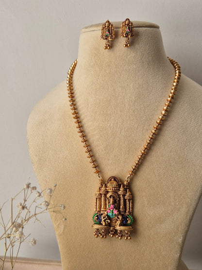 Close-up of the Devanshi Necklace Set: a gold-toned chain holding a large rectangular temple-style pendant with green and pink details, paired with matching small drop earrings by naitri.in