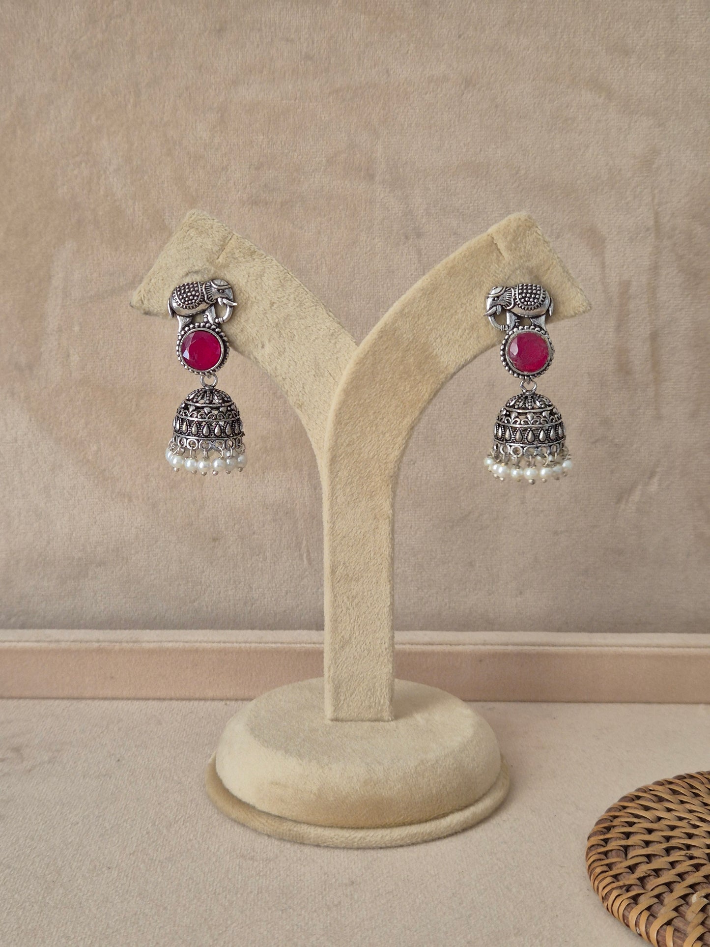 Pair of Devashri oxidized silver jhumka earrings featuring an elephant motif, pinkish-red stones, and white pearl drops by naitri.in