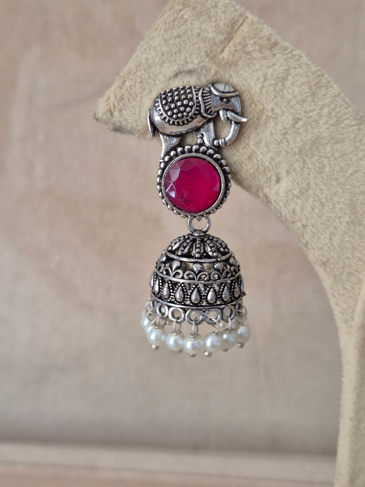 Handcrafted silver Jhumka earrings with vibrant red stones and small pearl beads hanging from an elephant design stud by naitri.in 