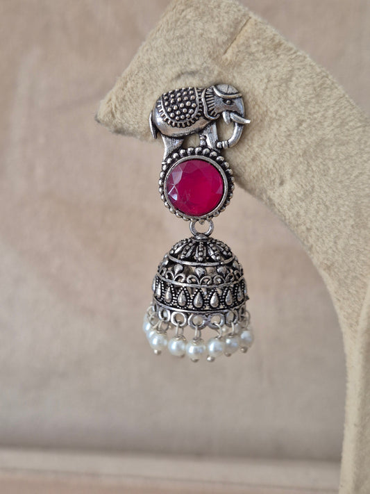 Handcrafted silver Jhumka earrings with vibrant red stones and small pearl beads hanging from an elephant design stud by naitri.in 