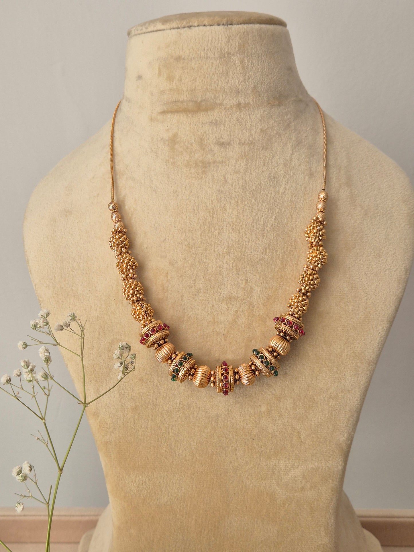 A handcrafted gold-polished brass strand necklace featuring intricate gold beads and alternating red and green stone accents by naitri.in