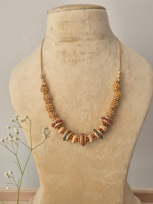 A handcrafted gold-polished brass strand necklace featuring intricate gold beads and alternating red and green stone accents by naitri.in