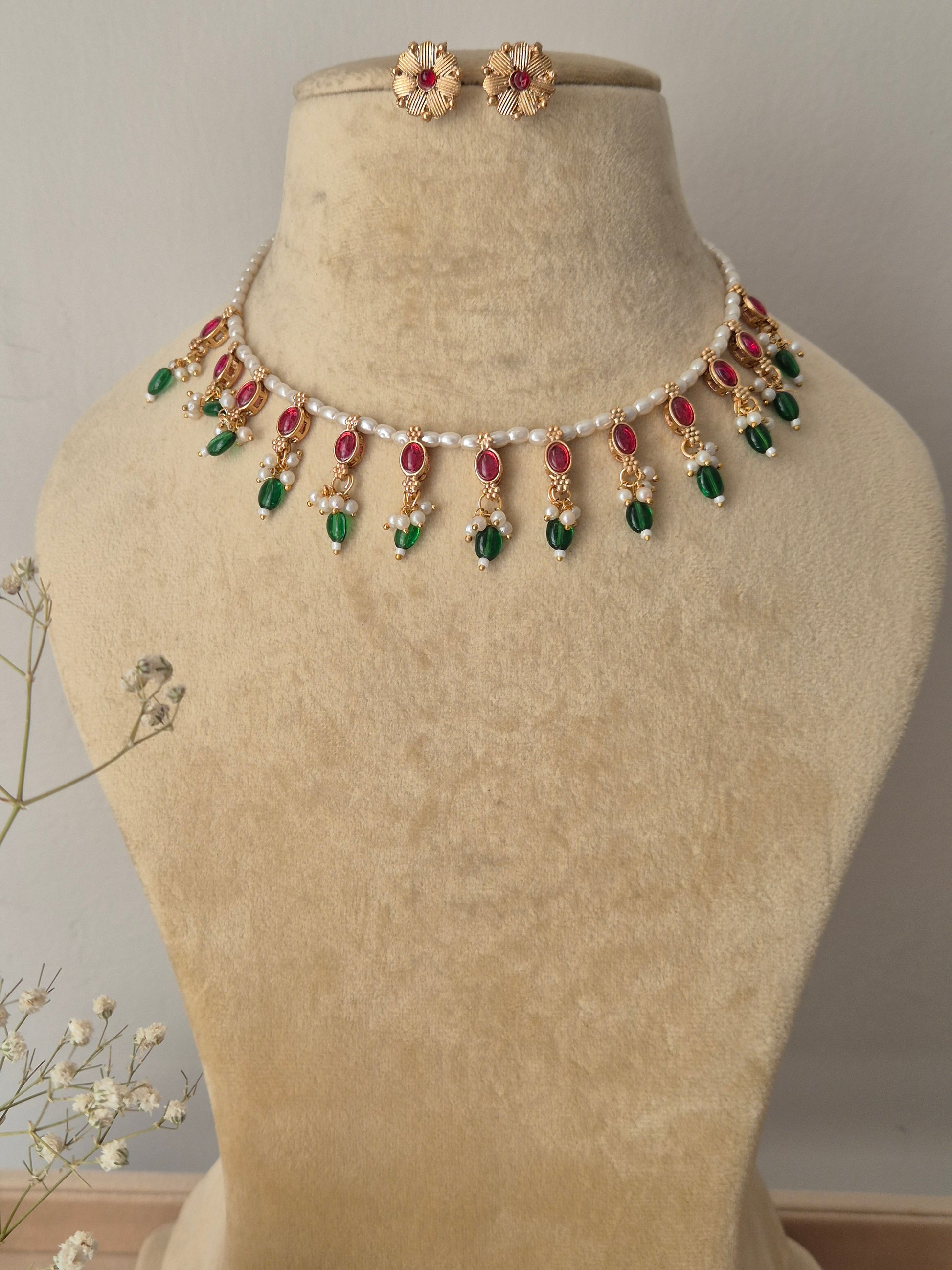 Handcrafted choker necklace featuring a delicate white pearl bead strand adorned with alternating ruby-red and emerald-green stone drops, paired with matching textured gold floral stud earrings by naitri.in