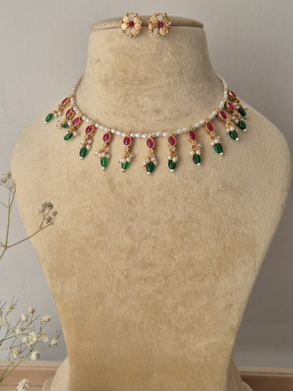 Handcrafted choker necklace featuring a delicate white pearl bead strand adorned with alternating ruby-red and emerald-green stone drops, paired with matching textured gold floral stud earrings by naitri.in